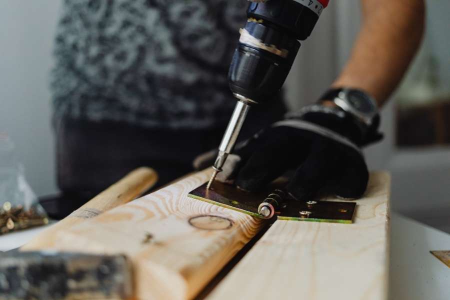 A woodworker drilling a screw into a metal hinge on a pine wood plank, a common step in biscuit joinery projects.