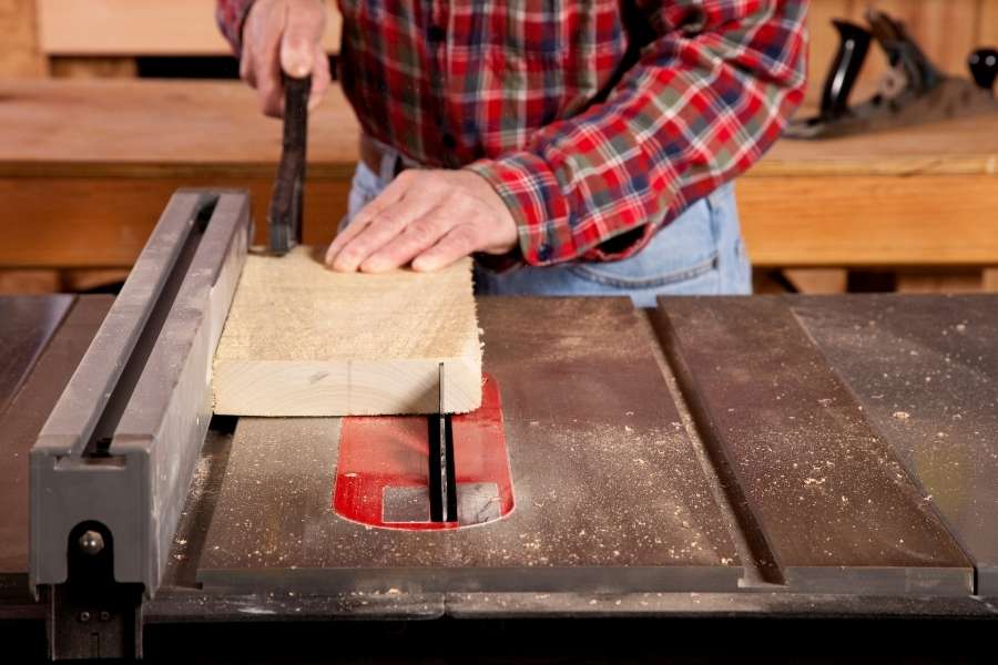 A woodworker operating a dangerous table saw without proper safety push sticks.